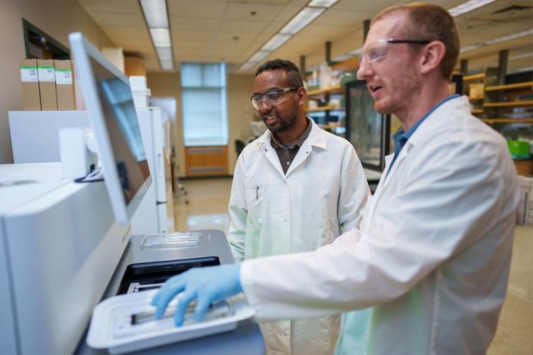在哈伯德基因组研究中心，两个人一起在测序机上工作的照片.